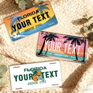 May include: Three Florida license plates with customizable text. One plate features a dolphin leaping from the ocean, another showcases palm trees at sunset, and the third displays oranges and blossoms. All plates read "Florida, Your Text, Sunshine State."