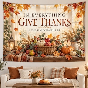 May include: A wall tapestry featuring a fall harvest scene with a wicker basket of pumpkins, apples, and wheat. The text reads IN EVERYTHING GIVE THANKS 1 THESSALONIANS 5:18. The scene includes a lantern, plaid fabric, and autumn leaves.
