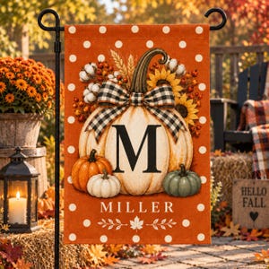 May include: A rectangular orange garden flag with white polka dots featuring a large central pumpkin with a black and white buffalo check bow, a letter M, and the name MILLER. The design includes smaller pumpkins, sunflowers, and cotton.