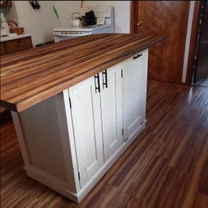 May include: A kitchen island with a butcher block countertop and white cabinet doors. The countertop is made of dark brown wood with lighter brown stripes. The cabinet doors have black handles.