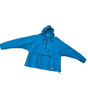 May include: Bright blue anorak jacket with a hood and a half-zip closure. The jacket features a front pocket with a black zipper and a drawstring at the hood. The sleeves are long and the jacket is made of a lightweight material.