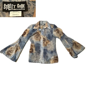 May include: A small, button-down blouse with bell sleeves. The blouse features a floral pattern in shades of blue, brown, and beige. The tag reads "STREET CODE" and "MADE IN U.S.A."