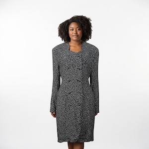 May include: A black and white floral print dress with long sleeves and a button-down front. The dress has a fitted silhouette and a knee-length hemline. The dress is worn by a person with dark curly hair.