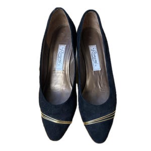 May include: A pair of black suede pumps with gold-colored trim. The shoes have a pointed toe and a low heel. The interior of the shoe is a light brown color. The brand name "Rangoni" is printed on a label inside each shoe.