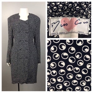 May include: A black and white dress with a geometric pattern. The dress has a collar and long sleeves. The label reads "Miss Co Co Paris Made in France".