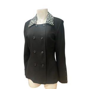 May include: Black double-breasted blazer with a leopard print collar. The blazer has six black buttons down the front and three buttons on each sleeve. The jacket is displayed on a mannequin.