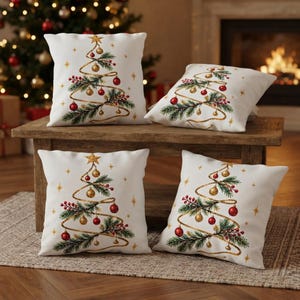 Puede incluir: Cuatro cojines cuadrados blancos con un diseño de árbol de Navidad estilizado. El árbol está formado por una cinta dorada en espiral decorada con ramas de pino verdes, bayas rojas, adornos rojos y dorados, y una estrella dorada en la punta.