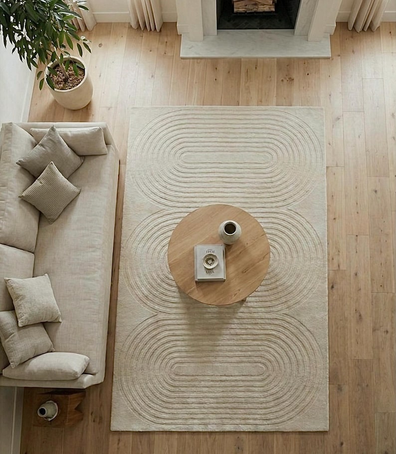 Neutral modern area rug hand tufted from premium wool in 8x10 dimension. The abstract curved motif creates movement while staying subtle and elegant. Photographed in a bright living space with beige sofa, wooden table, and fireplace. Excellent for homeowners seeking contemporary, Scandinavian, or organic modern decor with comfort and high end appeal.