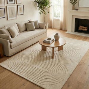 Hand tufted neutral wool rug in 8x10 size featuring a modern curved line pattern, styled in a bright minimalist living room. The beige and cream tones blend beautifully with a fabric sofa, wooden round coffee table, wall art, indoor plant, and fireplace. Thick plush texture offers softness and luxury, making it ideal for contemporary, Scandinavian, or Japandi interiors. Perfect large area rug for lounge, family room, or cozy apartment decor.