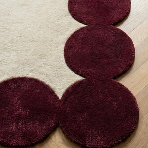 Large modern area rug in size 9x12 with sculpted burgundy perimeter and plush neutral interior. Ideal for open concept living rooms, this hand tufted carpet anchors furniture beautifully while adding warmth, comfort and high end visual appeal.