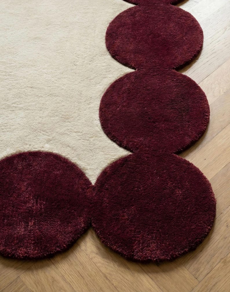 Large modern area rug in size 9x12 with sculpted burgundy perimeter and plush neutral interior. Ideal for open concept living rooms, this hand tufted carpet anchors furniture beautifully while adding warmth, comfort and high end visual appeal.
