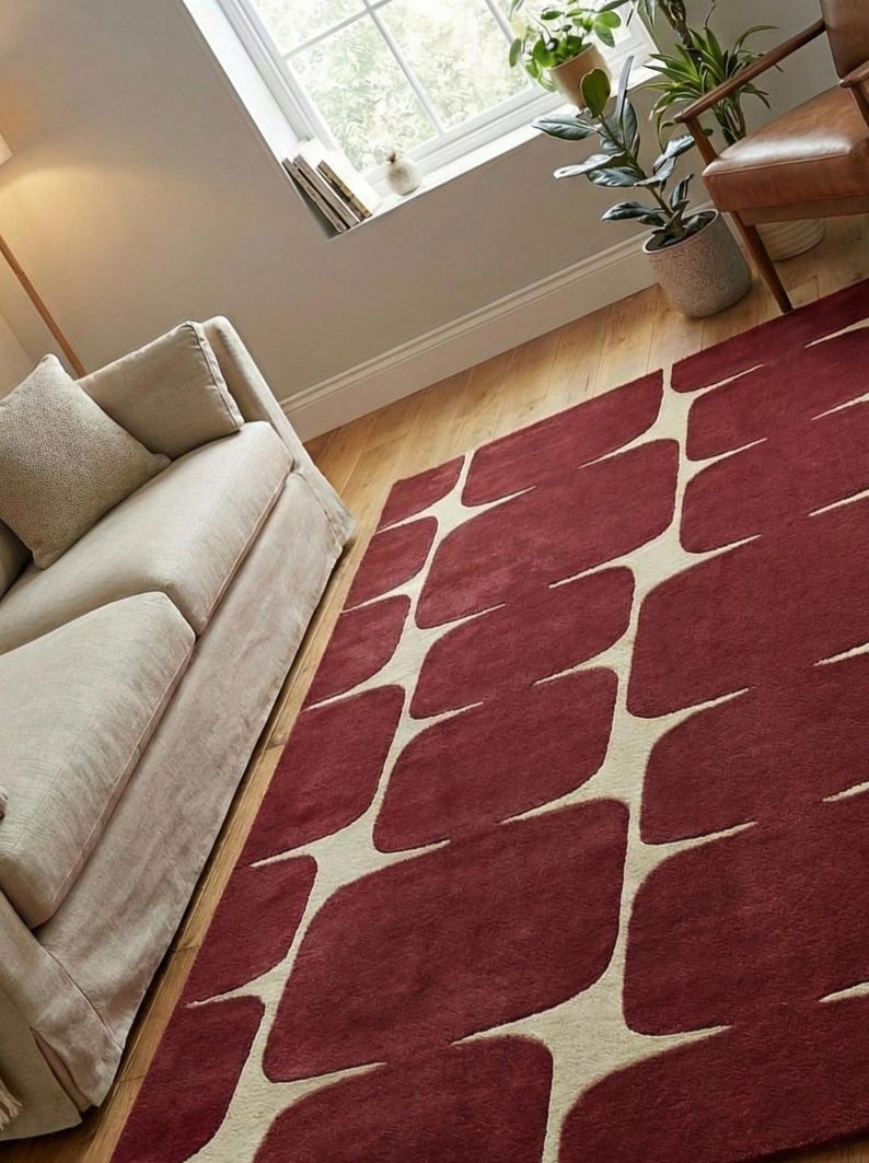 Luxury hand tufted geometric area rug in burgundy and ivory colors showcased in a minimal modern living room interior. This handmade wool rug features a unique abstract pattern that complements neutral furniture, wooden flooring, and indoor plants. Perfect for modern home decor, this soft and durable rug adds comfort, warmth, and visual interest to living rooms, bedrooms, apartments, and contemporary spaces.