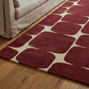 Abstract geometric hand tufted rug made from high quality wool, shown in a stylish living room with hardwood floors and minimalist furniture. The burgundy and cream color combination creates a bold yet elegant look, perfect for modern, contemporary, or mid century home decor. This handmade area rug adds warmth, softness, and a luxurious focal point to living rooms, bedrooms, and lounges.