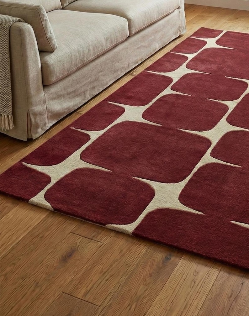 Abstract geometric hand tufted rug made from high quality wool, shown in a stylish living room with hardwood floors and minimalist furniture. The burgundy and cream color combination creates a bold yet elegant look, perfect for modern, contemporary, or mid century home decor. This handmade area rug adds warmth, softness, and a luxurious focal point to living rooms, bedrooms, and lounges.