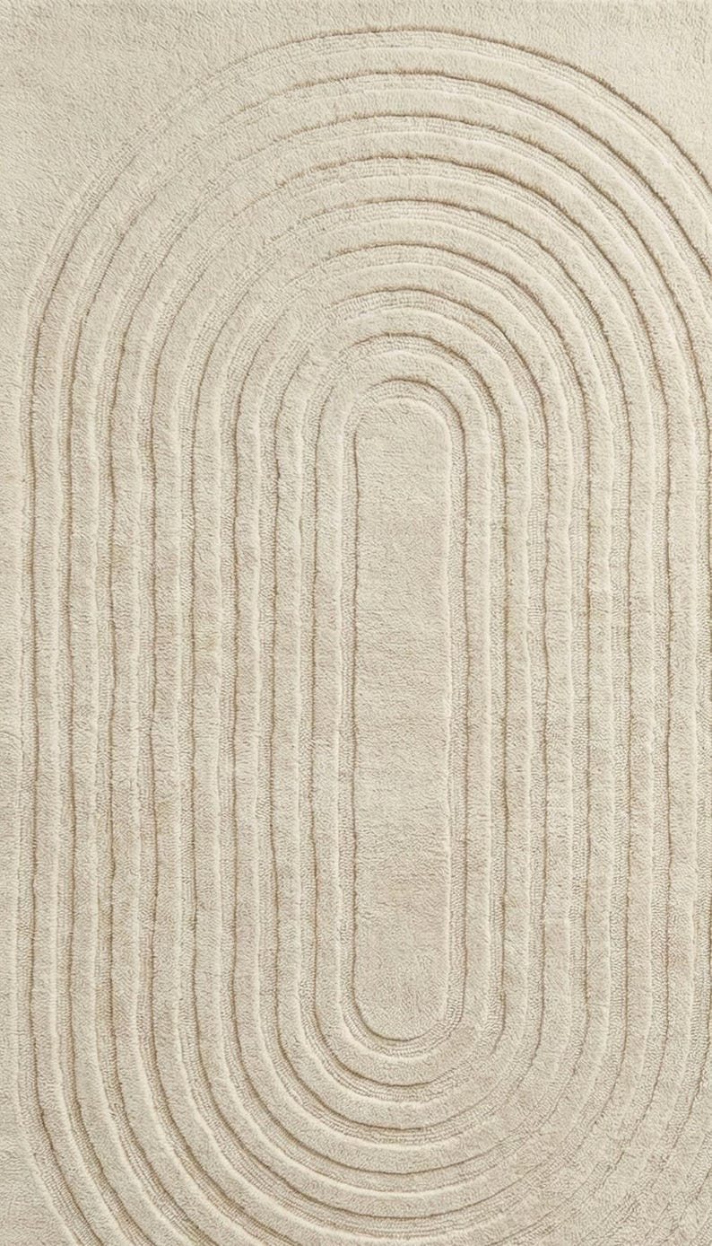 Large 8x10 hand tufted area rug in soft cream color with elegant abstract swirl lines. Placed under a modern wooden coffee table and neutral couch, this wool carpet enhances warm wooden flooring and airy spaces. Designed for minimalist and modern homes, the rug provides comfort, durability, and timeless style. Great choice for living room, bedroom, nursery, or reading corner needing a calm and sophisticated foundation.