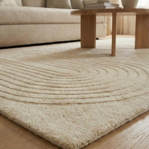 Modern beige hand tufted wool rug size 8x10 with raised curved pattern adding texture and depth. Styled in a Scandinavian inspired living room with light curtains, framed wall art, and natural greenery. The neutral palette complements contemporary furniture while creating a cozy atmosphere. Ideal large floor carpet for open spaces, under sofas, or statement decor in elegant and simple interiors.