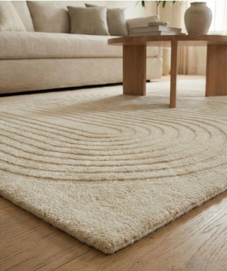 Modern beige hand tufted wool rug size 8x10 with raised curved pattern adding texture and depth. Styled in a Scandinavian inspired living room with light curtains, framed wall art, and natural greenery. The neutral palette complements contemporary furniture while creating a cozy atmosphere. Ideal large floor carpet for open spaces, under sofas, or statement decor in elegant and simple interiors.