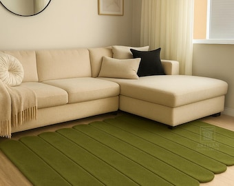 May include: A modern living room features a beige sectional sofa with decorative pillows and a green rug. The rug has a unique, elongated, rounded design. A round mirror and framed artwork adorn the wall.