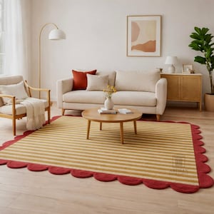 Op de afbeelding: Een rechthoekig tapijt met horizontale gele en witte strepen en een geschulpte rode rand. Het tapijt is geplaatst in een woonkamer met een bank, stoelen en een salontafel. Het tapijt heeft een decoratief ontwerp.