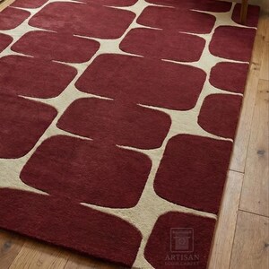 Modern hand tufted wool rug with bold geometric abstract design in rich burgundy color placed on a hardwood floor in a cozy living room setting. The rectangular area rug enhances the space with a luxurious handmade texture, soft wool feel, and artisan craftsmanship. Ideal for living room, bedroom, lounge, or office decor, this premium handmade rug blends contemporary style with timeless elegance.