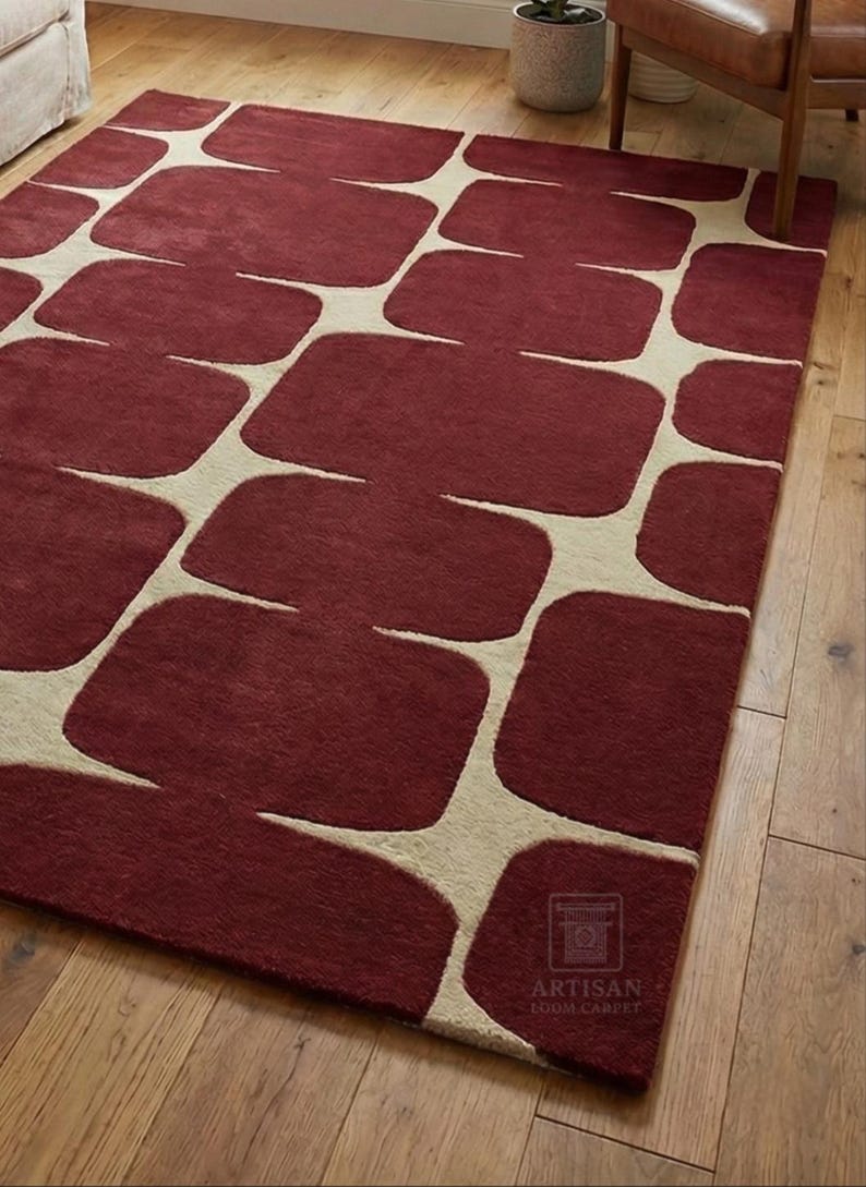 Modern hand tufted wool rug with bold geometric abstract design in rich burgundy color placed on a hardwood floor in a cozy living room setting. The rectangular area rug enhances the space with a luxurious handmade texture, soft wool feel, and artisan craftsmanship. Ideal for living room, bedroom, lounge, or office decor, this premium handmade rug blends contemporary style with timeless elegance.