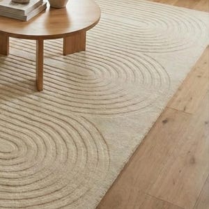 Beige wool hand tufted carpet 8x10 designed with flowing curved lines and plush texture. A perfect anchor for modern interiors, this large rug pairs effortlessly with neutral furniture and natural materials. Ideal for living rooms, bedrooms, studios, or calm relaxing environments. Adds warmth, sophistication, and a designer touch to everyday spaces.