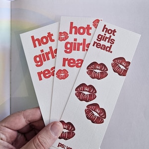 Könnte beinhalten: Drei weiße Lesezeichen mit rotem Text, der "hot girls read" lautet. Jedes Lesezeichen hat einen roten Lippenabdruck. Der untere Teil des Lesezeichens lautet "ps: you are hot."