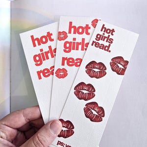 Könnte beinhalten: Drei rechteckige Lesezeichen aus weißem Papier mit dem roten Text "hot girls read." und verschiedenen roten Lippen-Illustrationen. Das rechte Lesezeichen enthält unten zusätzlich den roten Text "ps: you are hot.", alles auf strukturiertem Papier.