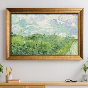 Puede incluir: Una pintura de paisaje enmarcada con un marco dorado cuelga sobre un mueble de madera clara. La pintura representa un campo verde bajo un cielo nublado. El mueble tiene una puerta corredera blanca y una puerta de panel tejido.