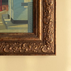 以下が含まれることがあります： 額縁に入った絵画のクローズアップ。フレームは装飾的で、濃い茶色のアンティーク仕上げです。絵画は、青と白のファサードを持つ建物を描いています。フレームの複雑な彫刻は、アートワークに優雅さを加えています。