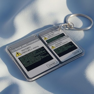 May include: A clear acrylic keyring with a silver ring. The keyring has a computer-themed design with the text "KEEPSAKES PHOTO.JPG is missing" in a window-like graphic. The design includes a warning symbol and a "Cancel" button.