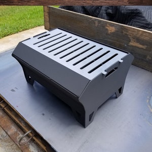 May include: A black metal fire pit with a rectangular shape and a grate on top. The fire pit is sitting on a metal surface. The text "DXF & SVG" is visible in the image.