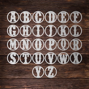 May include: A set of 26 metal letters in a circle, each letter is in a separate circle. The letters are in a white color and the background is a dark brown wood.