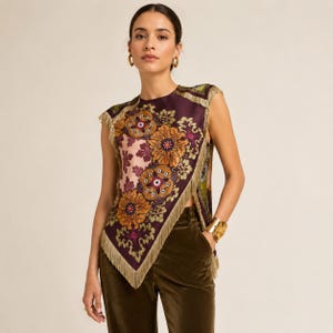May include: A sleeveless top featuring a deep purple base with a large, intricate floral pattern in shades of orange, gold, and pink. The garment has an asymmetrical hemline finished with long, light-colored fringe trim along the edges.