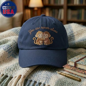 Può includere: Cappellino da baseball blu navy con ricamo di scimmie che si abbracciano e la scritta "You are never alone." Prodotto negli Stati Uniti.