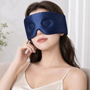 May include: A navy blue sleep mask with two eye cutouts. The mask is made of a smooth, silky material. The sleep mask is designed to block out light for better sleep.