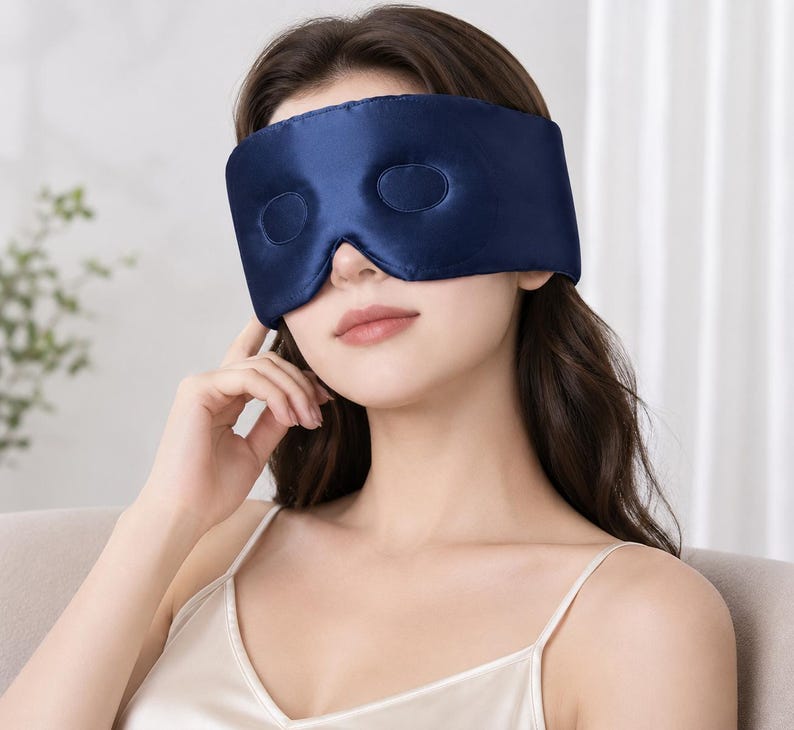 May include: A navy blue sleep mask with two eye cutouts. The mask is made of a smooth, silky material. The sleep mask is designed to block out light for better sleep.
