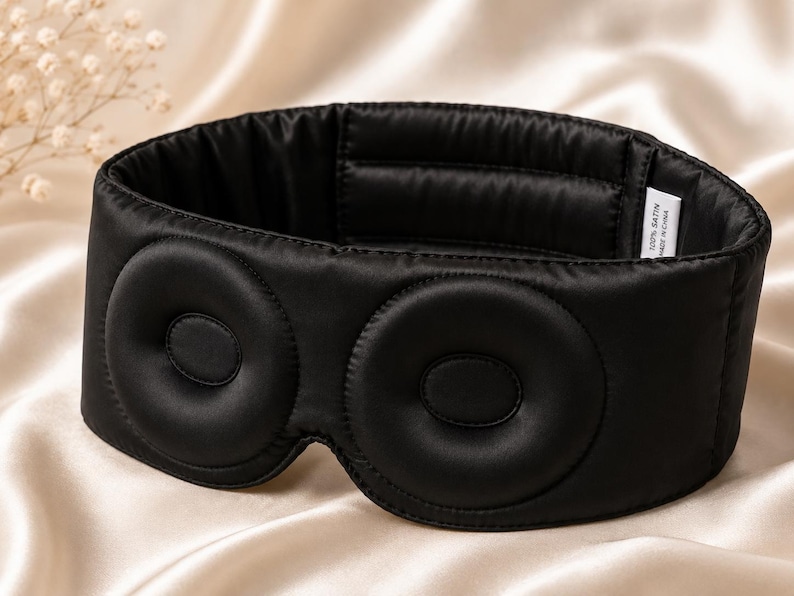 May include: A black satin sleep mask with two circular eye covers. The mask is designed to block out light and promote relaxation. The mask is made of 100% satin.