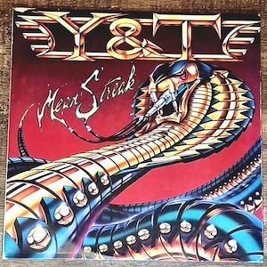 May include: Album cover for Y&T's "Mean Streak." The artwork features a stylized cobra with metallic gold, blue, and black scales against a red background. The band's name, "Y & T," is at the top, and the album title is in a cursive font.