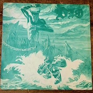 Könnte beinhalten: Ein quadratisches Schallplattencover in einfarbigem Türkis und Weiß mit dem Text DIO oben rechts und HOLY DIVER unten. Die Illustration zeigt eine gehörnte Figur, die eine Kette über einer in Meereswellen untergetauchten Person hält.