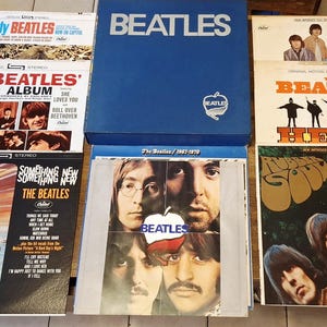 Op de afbeelding: Een verzameling vintage Beatles-albums, waaronder "The Early Beatles", "The Beatles' Second Album" en "Something New". Een blauwe boxset en andere albumhoezen zijn ook zichtbaar, met de iconische beelden en albumkunst van de band.