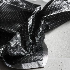 May include: A black fabric featuring a reflective, geometric, three-dimensional triangular pattern. The material has a glossy, metallic finish that catches the light, creating a textured, faceted appearance across the folded surface of the textile.