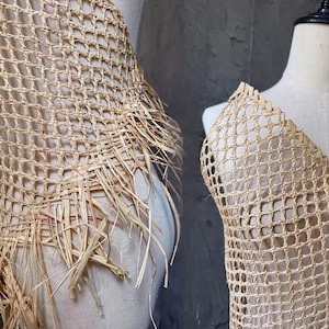 Könnte beinhalten: Zwei Stücke gewebten Baststoffs, präsentiert auf Schneiderpuppen. Der Stoff hat ein gitterartiges Muster mit ausgefransten Kanten in einem natürlichen Beige. Die Textur deutet auf eine handgefertigte oder handwerkliche Qualität hin, möglicherweise für Kleidung oder Dekorationen.