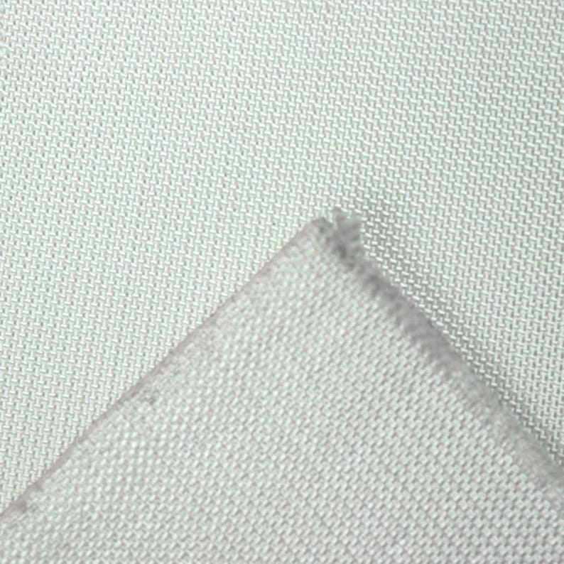 May include: Close-up of a light gray fabric with a woven texture. The corner of the fabric is folded over, revealing the edge. The fabric appears to be a light, neutral color.