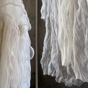 Puede incluir: Una tela blanca transparente con una textura delicada y arrugada y capas fluidas con volantes. El material es ligero y transl&uacute;cido, con pliegues suaves y ondulados que crean una sensaci&oacute;n de movimiento y profundidad en la superficie.