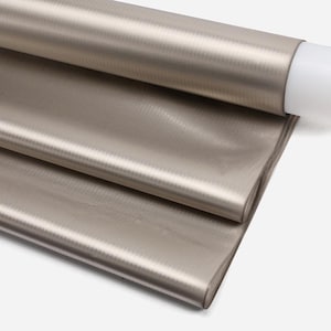 May include: A roll of metallic taupe fabric with a subtle, textured pattern. The fabric is partially unrolled, revealing layers of the material. The color is a muted, neutral tone, suitable for various crafting and design projects.
