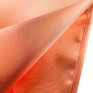 May include: Close-up of a folded, peach-colored fabric with a grid-like pattern. The fabric has a subtle sheen and appears to be lightweight. The edges are neatly sewn, suggesting a finished product.
