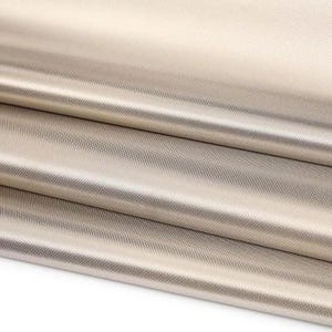 May include: Close-up of a stack of beige fabric with a subtle, textured pattern. The material is folded, revealing layers of the textile. The fabric has a slight sheen, reflecting light and creating highlights and shadows.