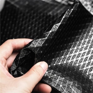 May include: A flexible black material featuring a repeating geometric pattern of small raised triangles. The surface is composed of interconnected black triangular segments with thin, reflective silver lines running between each individual shape.
