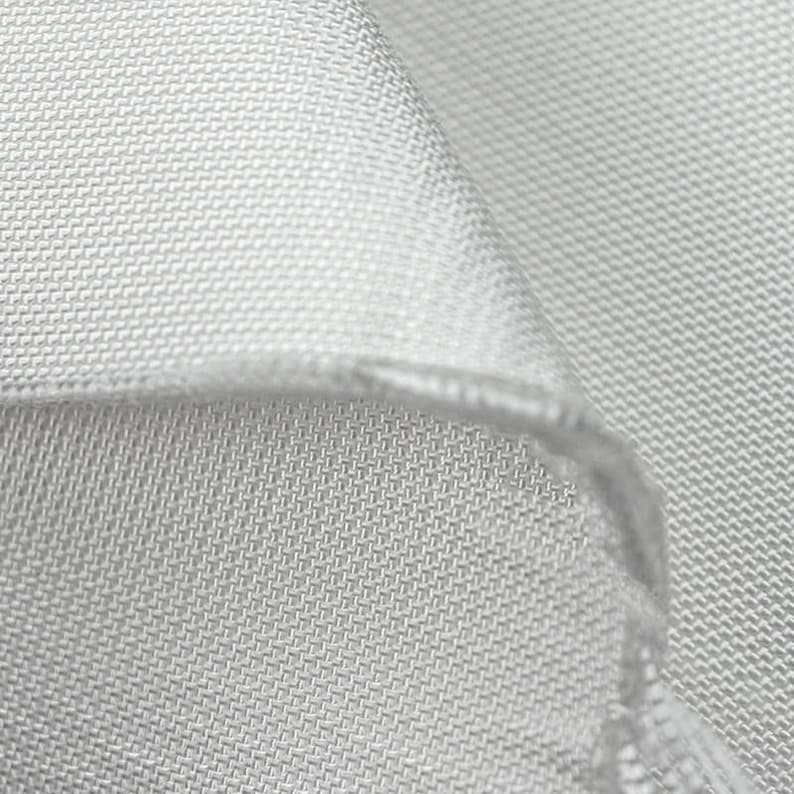 May include: Close-up of a light gray fabric with a woven texture. The fabric is folded over, revealing the edge and the intricate pattern of the weave. The material appears soft and smooth.